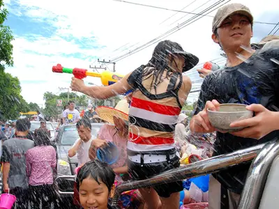 Man and woman with water guns and bowls in a Songkran street crowd