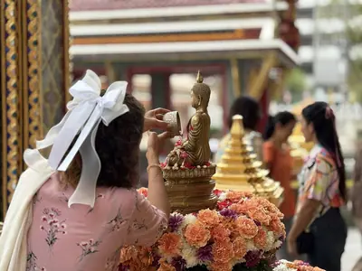 Woman in a pink top with a white bow pouring water over a small Buddha image during Songkran