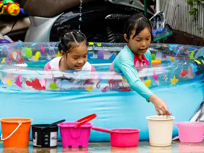 Two children splashing in a plastic paddling pool with colourful buckets during Songkran in Chiang Mai