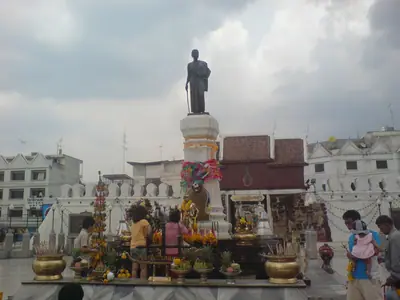 Het Ya Mo-standbeeld op zijn voetstuk voor de Chumphon-poort in Korat, met gelovigen en bloemoffers