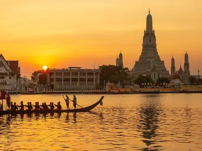 Royal barge procession with oarsmen passing Wat Arun at sunset on the Chao Phraya River in Bangkok