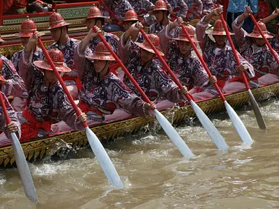 Oarsmen in red uniforms with raised oars aboard an escort barge
