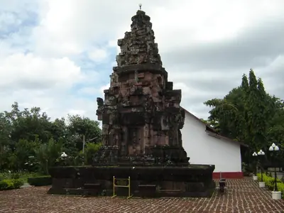 Wat Phra That Choeng Chum's reddish prang beside a temple building with a paved forecourt in Sakon Nakhon