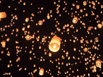 Glowing sky lanterns drifting against the night sky at Yi Peng, Chiang Mai