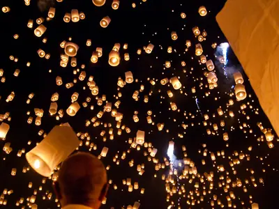 A person in the foreground releases a lantern among thousands in the night sky at the Yi Peng festival in San Sai near Chiang Mai