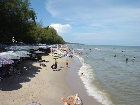 Strand van Cha-am met een zandstrook, parasols en zachte golven onder een gedeeltelijk bewolkte lucht