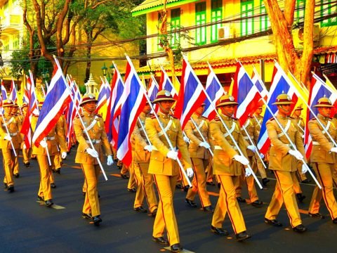 Soldaten in gele uniformen marcheren met Thaise vlaggen tijdens de kroningsviering van koning Rama X