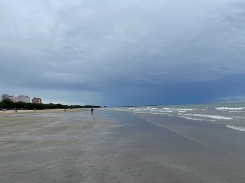 Breed, leeg strand van Hua Hin onder een bewolkte schemerlucht met de branding in de verte