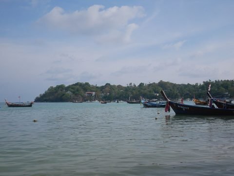Longtailboten afgemeerd in de baai bij Rawai Beach op Phuket, met een beboste landtong erachter