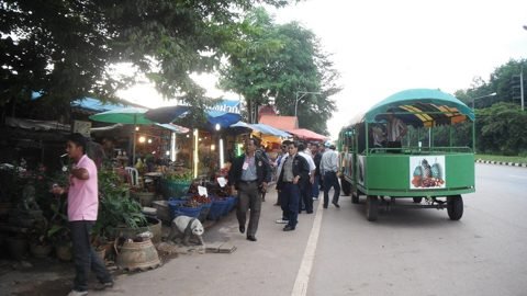 Fruitkraampjes langs de weg met tafels, luifels en een groene songthaew aan de Fruitweg in Rayong