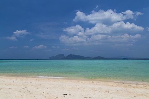 Wit zandstrand en turquoise water op Ko Kradan in Trang, met rotsachtige eilandjes aan de horizon